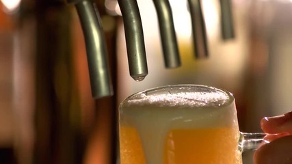 Overflowing glass of beer under tap. Tap beer dripping, slow-mo.