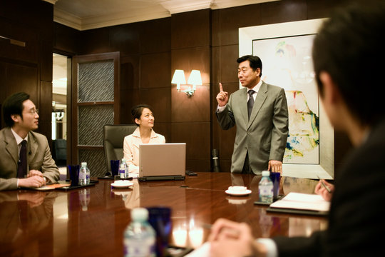 Mid-adult businessman standing presenting in a boardroom to colleagues.