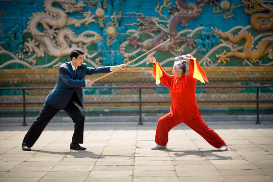 Mid-adult businessman and a senior woman performing traditional martial arts.