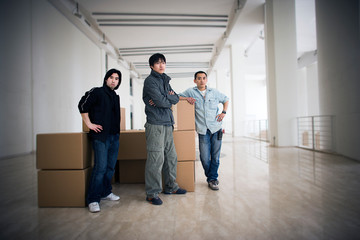 Portrait of three young men standing inside a large empty room.