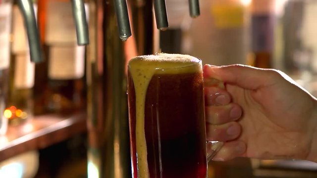 Dark beer glass with foam slowly dripping down. Hand scooping pint of beer under beer tap, slow-mo.