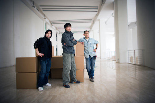 Portrait of three young men standing inside a large empty room.