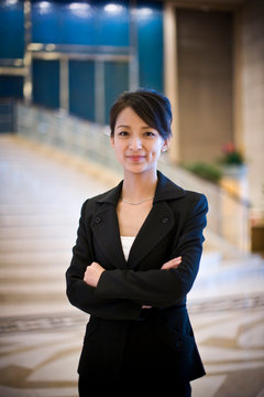 Portrait of a young adult woman with folded arms standing in the lobby of a building.