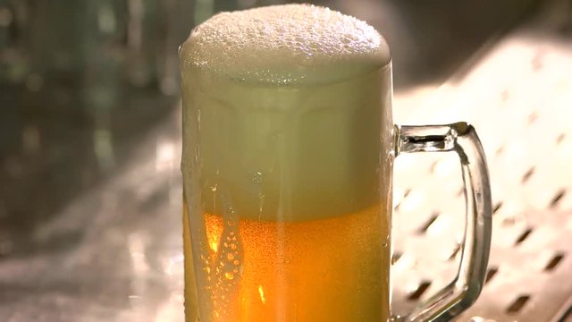 Overfilled dripping glass of beer on the bar table. Glass of draft beer half filled with froth, slow motion.