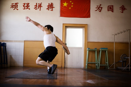 Teenage boy spinning while holding a weight in a gym.