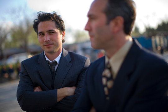 Young adult businessman standing outside with mid-adult colleague.