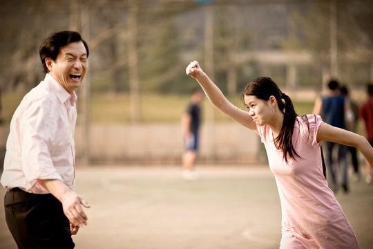 Mid-adult man having fun with his young adult daughter on a basketball court.