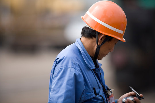 Mid-adult construction worker standing and using a cellphone on a wharf.