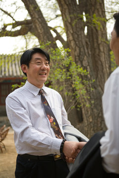 Mid-adult businessman greeting a colleague outside a building.