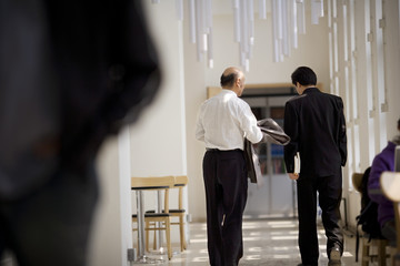 Mid-adult male teacher walking with a senior adult male colleague down a hall.