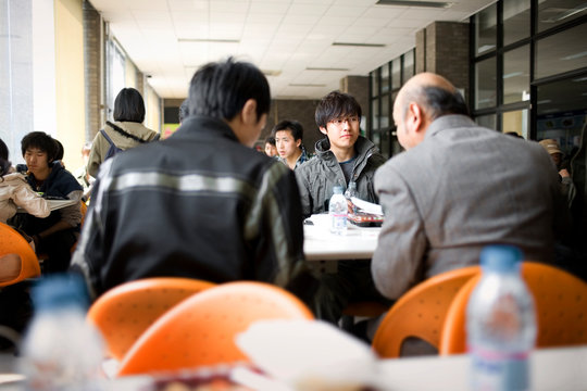 Teenage boy sitting in a cafeteria with friends and a senior male teacher.