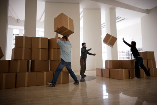 Three young adult men stacking boxes to carry.