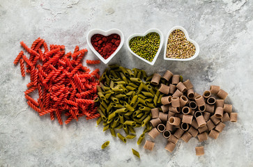 multicolor gluten-free pasta with ingredients in bowls in the form of hearts from which it is made on a stone table
