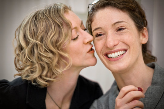 Smiling young woman being kissed by her girlfriend on the cheek.