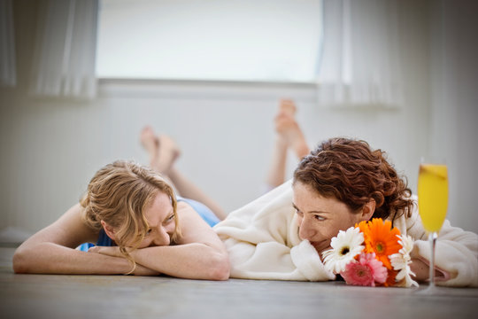 Happy lesbian couple lying on bare floorboards and looking at each other inside their home.