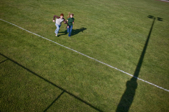 Young teenage couple running side by side across a sports playing field.