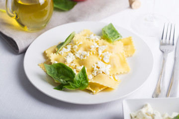 Boiled ravioli with basil, cheese and tomatoes on white table