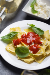 Boiled ravioli with basil, cheese and tomato sauce on a black background