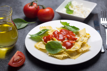 Boiled ravioli with basil, cheese and tomato sauce on a black background