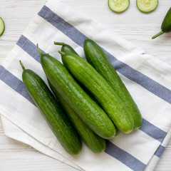 Fresh raw organic green cucumbers over white wooden surface, overhead view. Flat lay,  from above,...