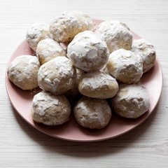 Homemade white mexican wedding cookies on pink plate over white wooden surface, side view.