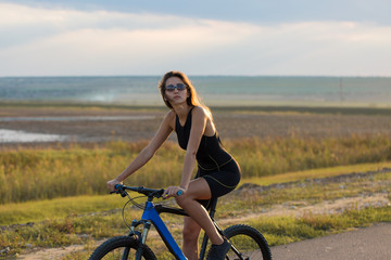 A girl riding a mountain bike on an asphalt road, beautiful portrait of a cyclist at sunset	