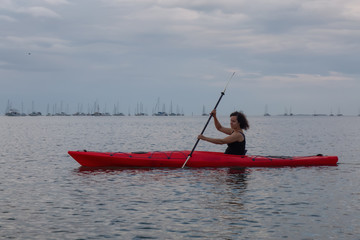 Adventurous girl kayaking in the Atlantic Ocean during a vibrant cloudy sunset. Taken in Key West, Florida Keys, United States.