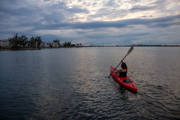 Adventurous girl kayaking in the Atlantic Ocean during a vibrant cloudy sunset. Taken in Key West, Florida Keys, United States.