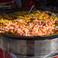 Street food in France, fresh prepared paella with rice and sea food in big pan on street market, ready to eat