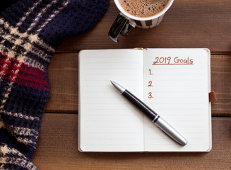 2019 goals list with notebook, cup of coffee over wooden desk.