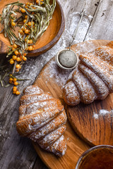 Fresh baked traditional croissant on wooden slate serving board with berries on white cloth napkin over dark brown texture background.