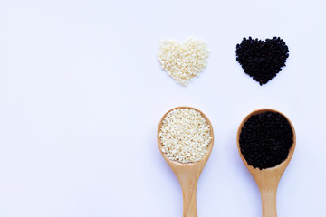 Black and white sesame seeds on wooden spoon, white background.