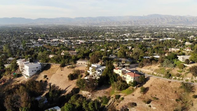 Epic aerial view flying along a hill ridge with a car and the San Fernando Valley in the background.