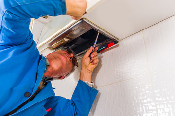 Obraz premium Senior craftsman fixing the kitchen fan in apartment