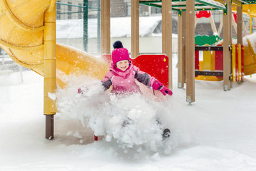 Little cute baby girl having fun on playground at winter. Children winter sport and leisure outdoor activities