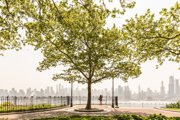 Fototapeta premium New York City midtown Manhattan skyline panorama view from Boulevard East Hamilton Park over Hudson River. Big tree in Hamilton Park promenade.