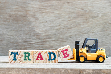 Toy forklift hold letter block e to complete word trade on wood background