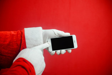 Santa showing mobile phone during holiday time, mockup electronic communications technology equipment background. Closeup image of hands working with video or photography on smart telephone.