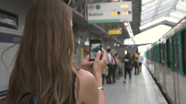 Over the shoulder portrait of a young beautiful woman take a photo with her phone as a train arrives in the city 