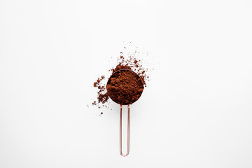 Rose gold measuring cup of cocoa powder on a white background, healthy food concept
