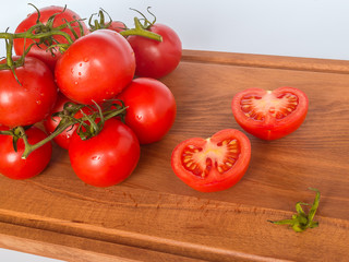 Red ripe tomato branch on a brown wooden cutting board on a neutral background. Healthy eating and vegetarian food concept, close up, selective focus.