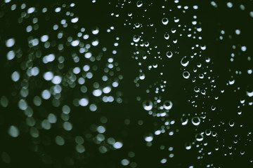 Naklejka na ściany i meble Dirty window glass with drops of rain. Atmospheric green background with raindrops in bokeh. Droplets and stains close up. Detailed transparent texture in macro with copy space. Rainy weather.