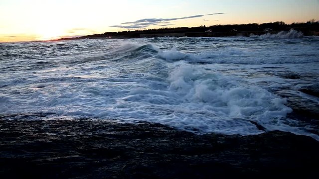 Roaring waves from the Atlantic ocean crash against the shores of Cape Cod during sunset in the fall.