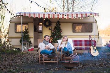 Beautiful young couple sitting in the chair in the background of a camper van in the autumn day