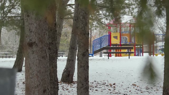 A kids playground sits in a snowy forest. Camera moves around a la Peeping Tom.
