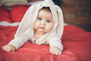 Smiling cute baby child in rabbit costume lying on red bed near Christmas tree