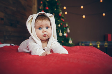 cute baby child in rabbit costume lying on red bed near new year tree