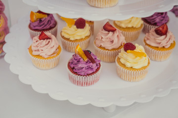 Sweet cupcakes with cream custard and berries on the festive table of candy bar. Sweets on a buffet table. 