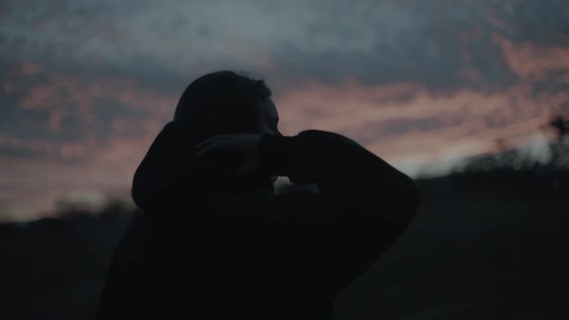 A woman removes her hood dramatically as the sun sets beautiful behind her.