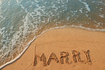 The word marry handwriting on sand beach with blue waves background.